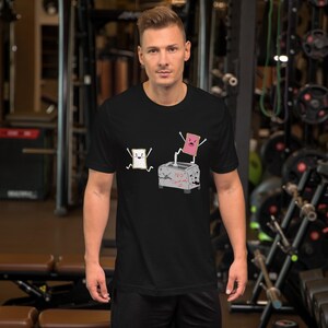 以下が含まれることがあります： 黒いTシャツ。トースターと2枚のトーストの漫画デザイン。1枚は白、もう1枚はピンク。トースターには「NO Toasting」と書かれています。楽しくて風変わりなデザインです。
