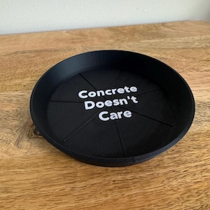 May include: A black, round tray with the text "Concrete Doesn't Care" in white. The tray has a segmented design and is sitting on a wooden surface.