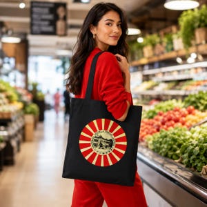 May include: A black tote bag featuring a circular graphic with red and cream radiating stripes. The center of the circle displays a black and white illustration of a building with the text "IMPERIAL HOTEL TOKYO JAPAN" printed around the border.
