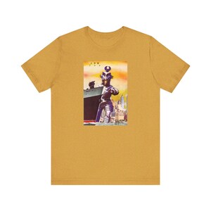 May include: A yellow t-shirt with a vintage illustration of a giant robot standing in front of a ship and city skyline. The text on the image reads "人魚  7-7-7".