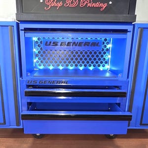 Könnte beinhalten: Eine blaue US General Werkzeugkiste mit offenen Türen. Die Kiste hat Schubladen und einen beleuchteten Innenraum. Auf der Oberseite der Kiste steht der Text "zshop 3D Printing". Die Kiste steht auf Rädern.