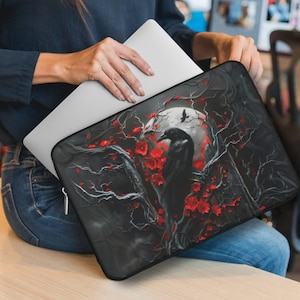 May include: Black laptop sleeve with a raven perched on a branch with red flowers and a full moon in the background.