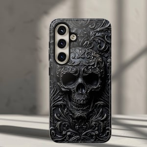 May include: Black phone case featuring a detailed skull design with floral accents. The case has a three-lens camera cutout and a dark, textured appearance. The skull is the central focus, with intricate carvings.