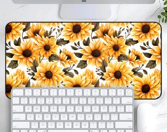 May include: A white desk mat with a repeating pattern of yellow sunflowers on a white background. The mat is placed on a white surface with a keyboard and mouse.