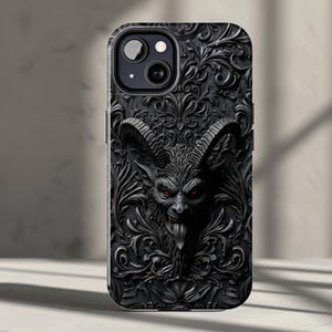 May include: Black phone case featuring a detailed, embossed design. The case showcases a demonic figure with red eyes, horns, and a long tongue, set against a backdrop of ornate floral patterns. The case is designed for a smartphone.