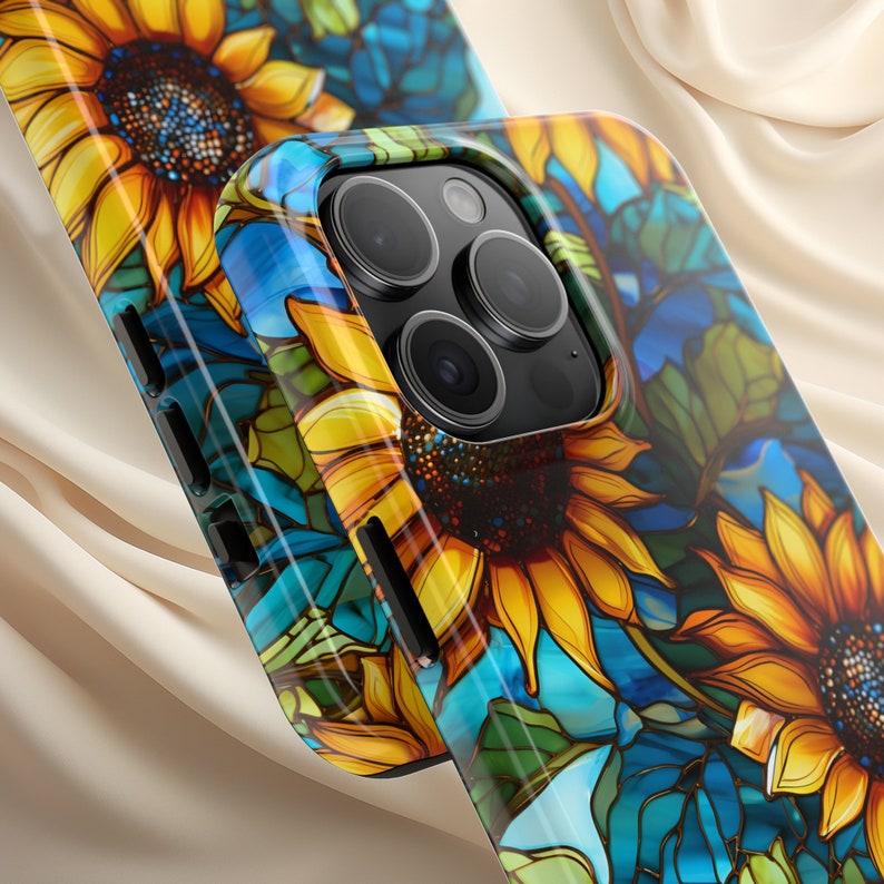 May include: A phone case with a colorful stained glass design featuring sunflowers and blue accents. The case has a raised camera bump and a black border.