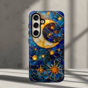 May include: A phone case with a stained glass design featuring a crescent moon, a sun, and stars on a blue background.