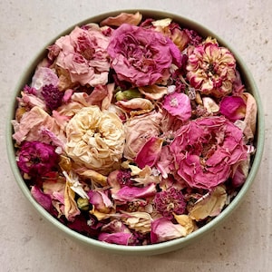 Op de afbeelding: Een ronde, lichtgroene kom gevuld met een verzameling gedroogde bloemblaadjes en hele gedroogde rozenbloesems in diverse tinten roze, magenta, crème en wit. Het mengsel bevat compacte rozenknoppen en losse, delicate bloemblaadjes.