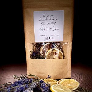 May include: A brown paper pouch with a clear window containing dried lemon slices and lavender. The label reads Organic Lavender & Lemon Summer Pot, Handmade in Somerset, Just Forage Then. Dried lavender sprigs and lemon slices are in front.
