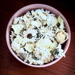 May include: A pink bowl filled with dried white flowers and rose petals. The flowers are arranged in a bouquet-like shape and include roses, daisies, and other varieties.