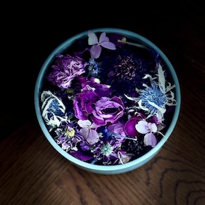 May include: A blue bowl filled with dried purple and blue flowers. The flowers are arranged in a random pattern and include roses, thistles, and other varieties.