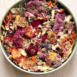 Può includere: Una ciotola rotonda verde chiaro riempita con una densa miscela di petali di fiori essiccati ed elementi botanici. L'assortimento comprende varie tonalità di magenta intenso, arancione brillante, giallo tenue e fiori e fogliame essiccati color crema.