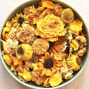 May include: A round, light green bowl filled with a collection of dried yellow flowers, including roses, daisies, and various petals. The arrangement features diverse textures and shades of yellow, ranging from pale cream to deep golden hues.