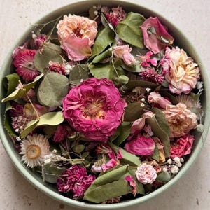 Peut inclure: Un bol rond vert clair rempli d'un assortiment de fleurs et de feuillages séchés. La composition comprend des roses magenta vives, des boutons de rose rose pâle, des immortelles blanches et des feuilles d'eucalyptus vertes et texturées.