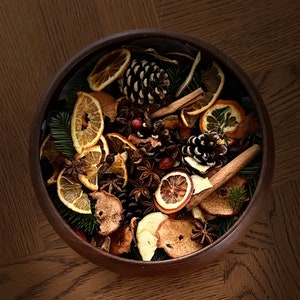 May include: A wooden bowl filled with a variety of dried fruits, spices, and pine cones. The bowl is filled with orange slices, cinnamon sticks, star anise, and other spices.