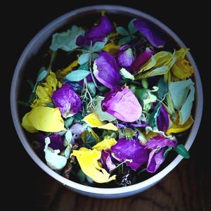 May include: A white bowl filled with dried flower petals in shades of yellow, purple, and green.