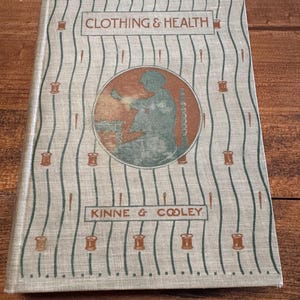 May include: A vintage book titled "Clothing & Health" by Kinne & Cooley. The cover features a brown and green illustration of a person sewing with a spool of thread.