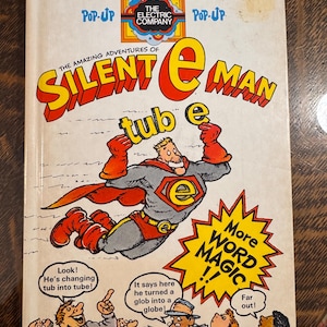 May include: A vintage pop-up book titled "The Amazing Adventures of Silent E Man." The cover features a cartoon superhero with the letter "e" on his chest, and the words "More Word Magic!!" are in a yellow burst.