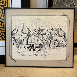 May include: A black and white illustration of a group of crayfish sitting at a table with chairs. The crayfish are wearing glasses and have human-like expressions. The text "The Crawfish Patio" is written in a bold font above the crayfish. The caption below the crayfish reads "Had any tails lately?"