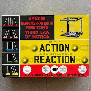 May include: A vintage educational toy box with the text "AMAZING DEMONSTRATION OF NEWTON'S THIRD LAW OF MOTION." The box features diagrams and a depiction of a Newton's cradle. The text "ACTION" and "REACTION" are also displayed.