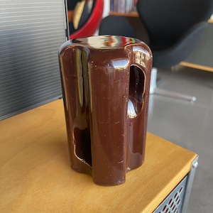 May include: A dark brown ceramic insulator with a hole in the center. The insulator is shaped like a cylinder with a rounded top and bottom.