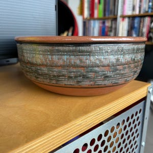 May include: A large, round, terracotta-colored bowl with a black and white striped design. The bowl has a glossy finish and is sitting on a wooden surface.