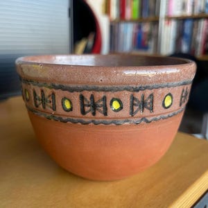 Puede incluir: Un cuenco de terracota con un diseño geométrico negro y amarillo alrededor del borde.