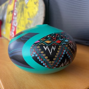 May include: A teal ceramic bowl with a black and white geometric design. The bowl has a colorful pattern on one side, featuring red, yellow, blue, and green accents.
