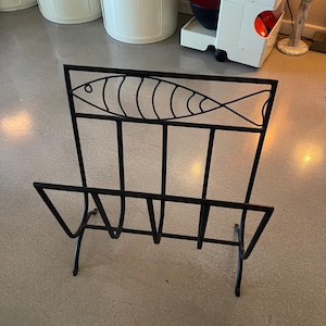 May include: Black metal magazine rack with a stylized fish design. The rack has four tiers for holding magazines or newspapers.