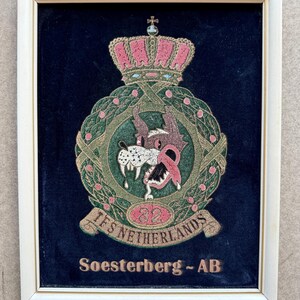 May include: Framed embroidered emblem with a white frame. The emblem features a pink crown, a wolf-like creature, and the text "IFS NETHERLANDS" and "Soesterberg - AB". The background is dark blue.