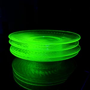 May include: A stack of three green glass plates with a spiral design. The plates are illuminated, creating a bright, neon green glow against a black background. The plates' reflection is visible below.