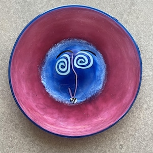May include: A red and blue glass bowl with a swirling design in the centre. The bowl has a dark blue rim.