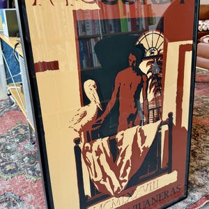 May include: Framed art print with the word "McCurdy" at the top. The artwork shows a person, a pelican, and a balcony scene. The text "OBRAS SANJUANERAS" is at the bottom. The colour scheme includes beige, brown, and black.