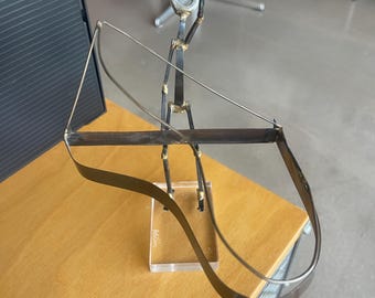 Könnte beinhalten: Eine Metallskulptur einer Person, die ein Saiteninstrument spielt. Die Figur besteht aus geschweißten Metallstäben und hat ein minimalistisches Design. Das Instrument hat einen gebogenen, dunkelbraunen Korpus und ist auf einem transparenten Acrylsockel montiert.