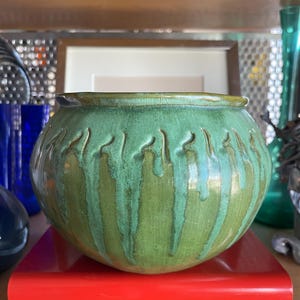 May include: A green ceramic planter with a textured, drippy glaze. The planter is round and has a wide opening.