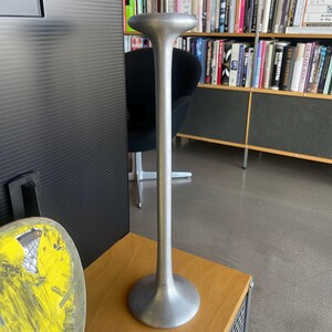 May include: A silver metal candlestick with a tall, slender stem and a wide, flared base.