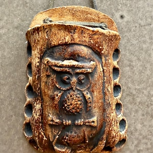 Op de afbeelding: Een bruine keramische uilvormige wandzak met een getextureerd oppervlak. De uil heeft grote ogen en een gedetailleerd veermotief. De zak heeft een lus om op te hangen en decoratieve gaten aan de zijkanten.