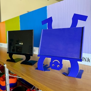 Peut inclure: Un porte-enseigne rectangulaire noir avec une base plate et un porte-enseigne rectangulaire bleu doté d'une tête de robot avec un visage souriant en bas. Le support bleu est positionné avec la tête du robot tournée vers le bas.