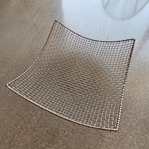 May include: A square-shaped wire mesh basket with a metallic silver finish. The basket features a grid pattern constructed from thin metal wires, with a thicker wire frame forming the edges and a slightly concave, curved shape throughout.