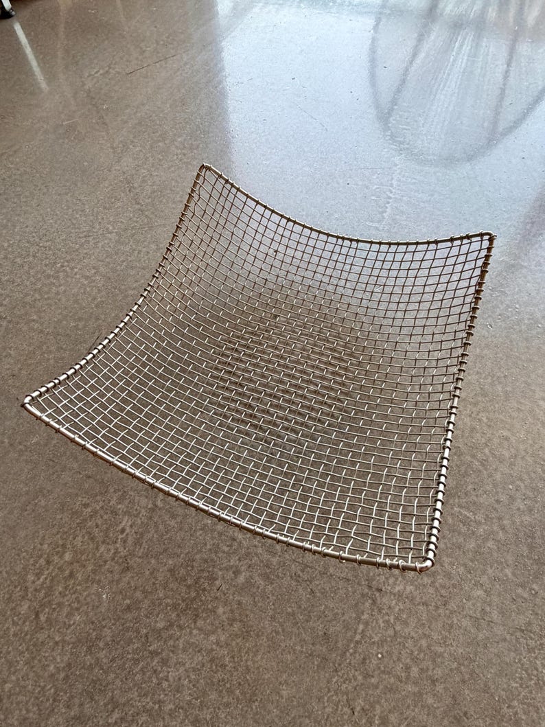 May include: A square-shaped wire mesh basket with a metallic silver finish. The basket features a grid pattern constructed from thin metal wires, with a thicker wire frame forming the edges and a slightly concave, curved shape throughout.