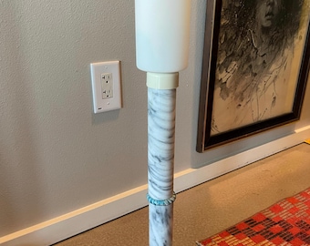 May include: A floor lamp featuring a cylindrical white frosted glass shade atop a tall, slender column base made of white marble with grey veining. The base includes a circular marble foot and a small, decorative turquoise-coloured ring accent.