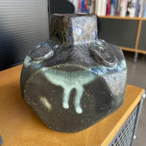 Op de afbeelding: Een donkerbruine keramische vaas met een geometrische vorm en blauwe en witte glazuur. De vaas heeft een uniek, abstract ontwerp.