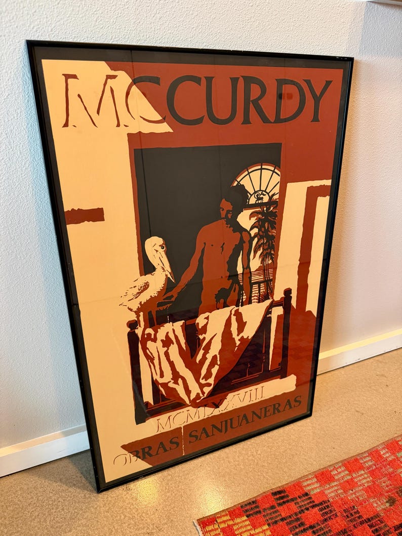 May include: Framed art print with the name "MCCURDY" in large letters. The artwork shows a person in a window with a bird, with the text "OBRAS SANJUANERAS" and "MCMXVIII" at the bottom. The color scheme includes beige, brown, and black.