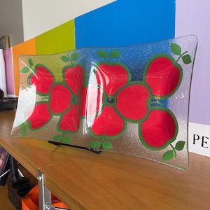 May include: A clear glass serving dish with a red and green floral design. The dish has a textured surface and is divided into two sections.