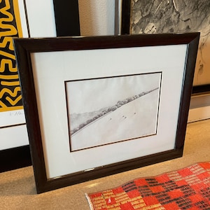 May include: A framed black and white drawing of a landscape with a row of trees and a few sheep in the distance. The drawing is on a white background and is framed in a dark wood frame.