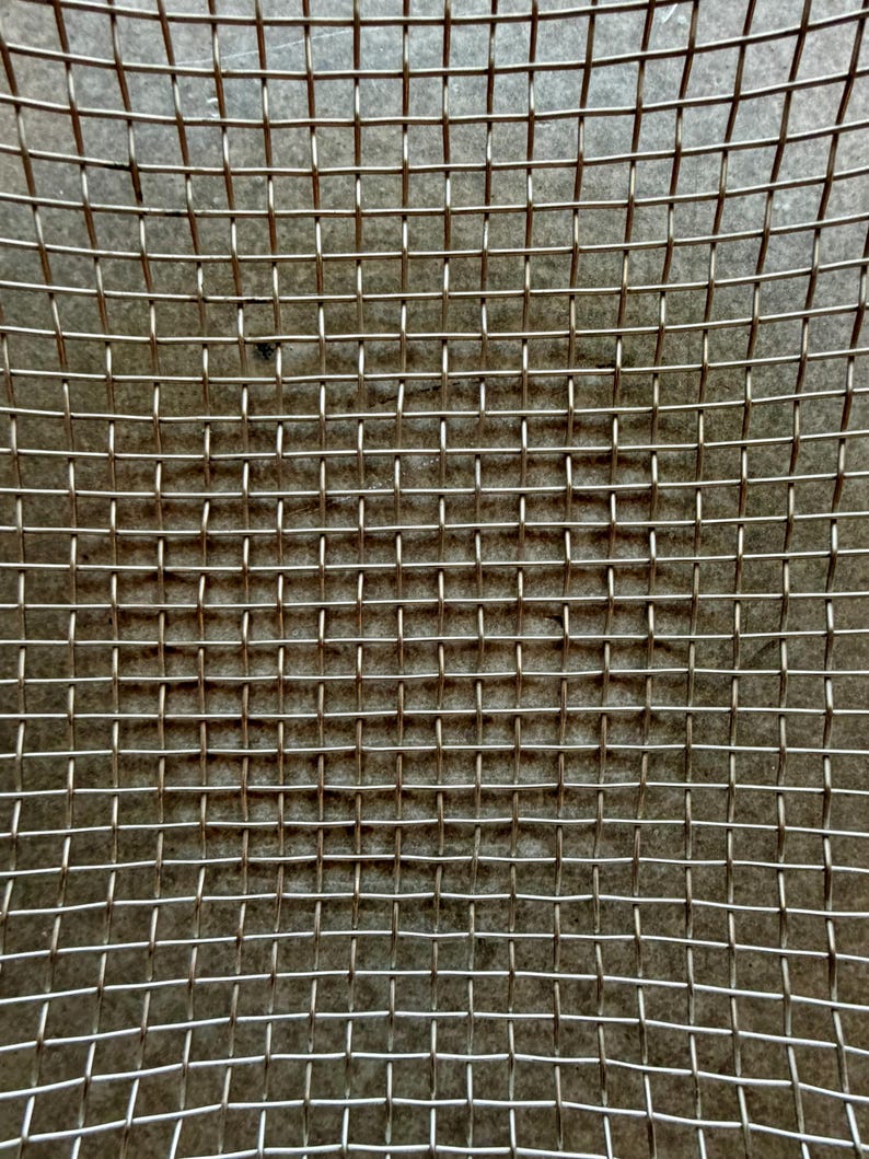 May include: A metallic wire mesh screen featuring a uniform grid pattern of intersecting silver-toned wires. The structure consists of evenly spaced horizontal and vertical strands creating a series of small, square-shaped openings throughout the surface.