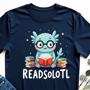 May include: A navy blue t-shirt with a cartoon axolotl wearing glasses and reading a book. The axolotl is sitting on a stack of books. The text "READSOLOTL" is printed below the axolotl.