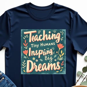 May include: Navy blue t-shirt with a graphic design that says "Teaching Tiny Humans Inspiring Big Dreams". The graphic is surrounded by colorful flowers.