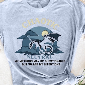 May include: A light blue t-shirt with a graphic of a dragon flying in front of a moon and clouds. The text "Chaotic Neutral" is above the dragon and the text "My methods may be questionable but so are my intentions" is below the dragon.