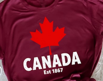 May include: A maroon t-shirt with a white graphic of a red maple leaf and the text "CANADA Est 1867".